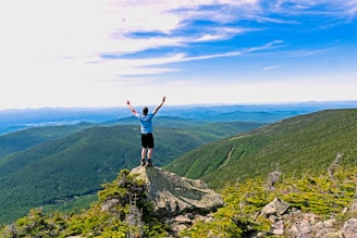 man raising his hands standing on mountain range