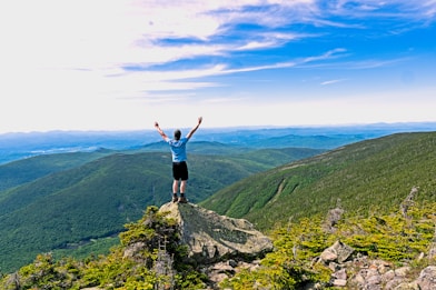 man raising his hands standing on mountain range