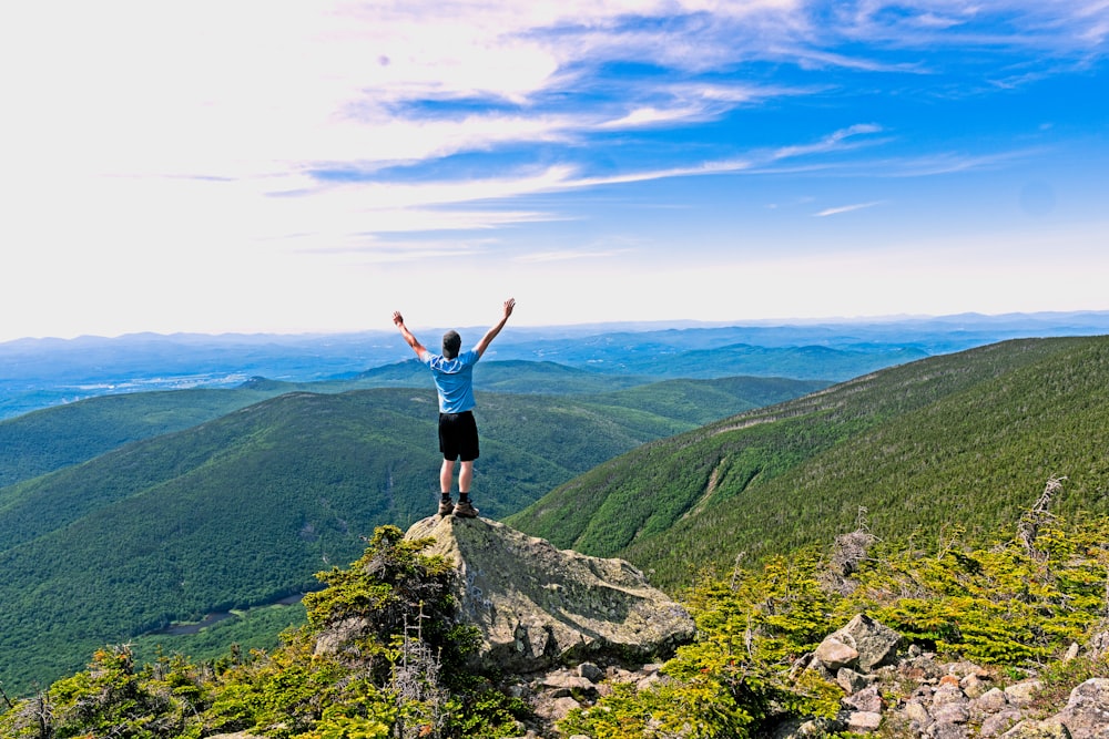 man raising his hands standing on mountain range