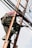 A person is climbing a ladder while working on electrical or communication cables. They are wearing work boots and protective gear, including knee pads, and have a harness for safety. Various cables are intertwined around the ladder.