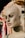 A mannequin head with a smooth, painted complexion and detailed facial features, including defined eyebrows and large, expressive eyes. It is situated against a backdrop of various colorful fabrics and textiles that hang on a rack.