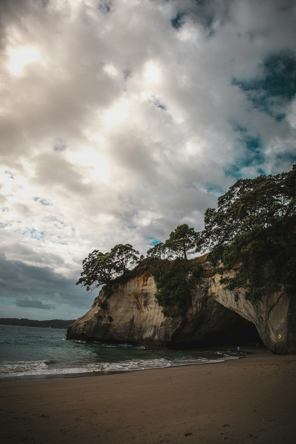 rock formation surrounded by trees near body of water under cloudy sky at daytime