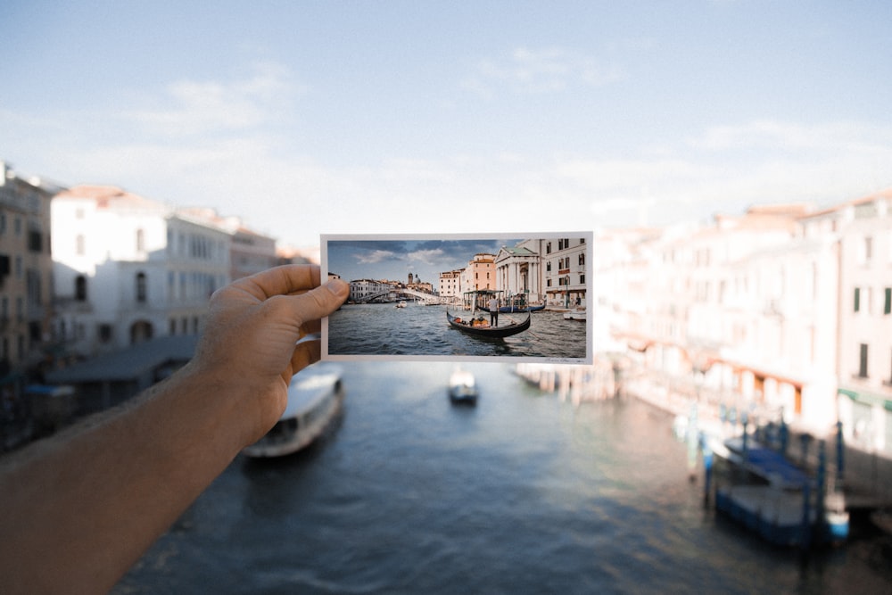 Persona che tiene la foto della barca sullo specchio d'acqua