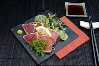 tuna with lemon and greens salad on black plate