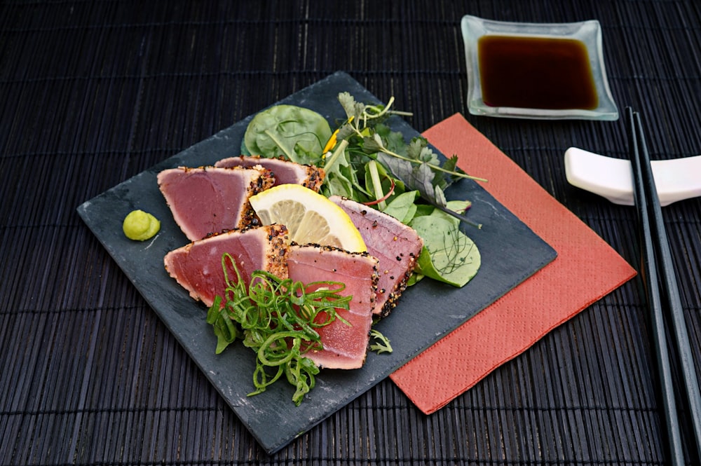 tuna with lemon and greens salad on black plate