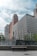 A cityscape with modern high-rise buildings, one of which has the logo of a well-known bank. A large, tiered fountain is in the foreground, with water cascading down its steps. The background features a tall building topped with an American flag.