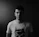 Portrait of a young man wearing a black oversized Velmora Paris t-shirt with a bold back print, standing against a smoky urban backdrop.