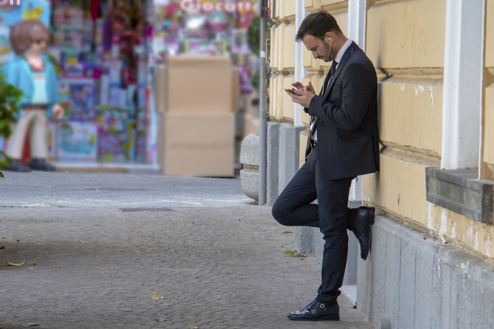 man holding his phone while leaning on building
