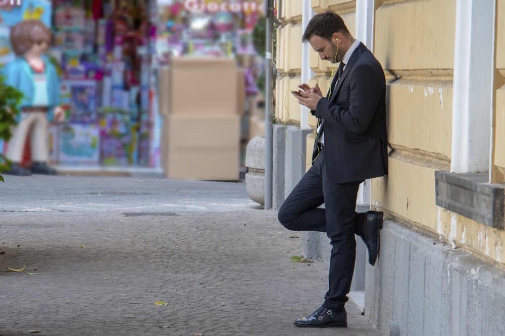 homem segurando seu telefone enquanto se apoia no prédio