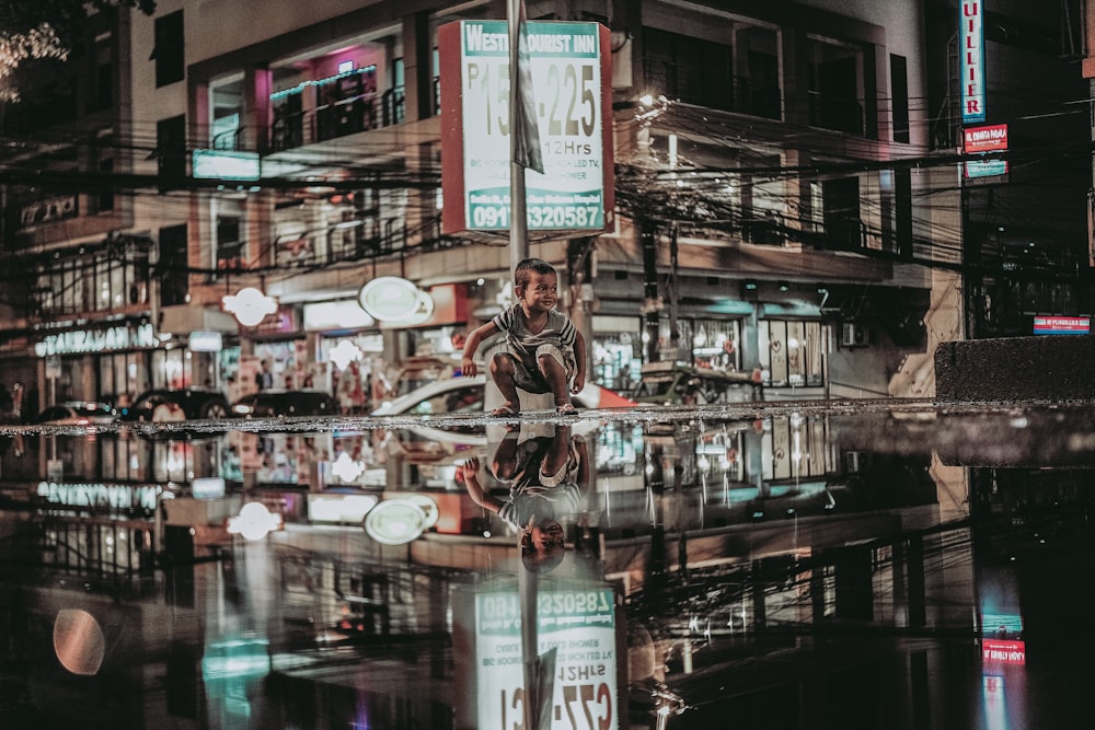 reflection photography of boy sitting beside pole near restaurant