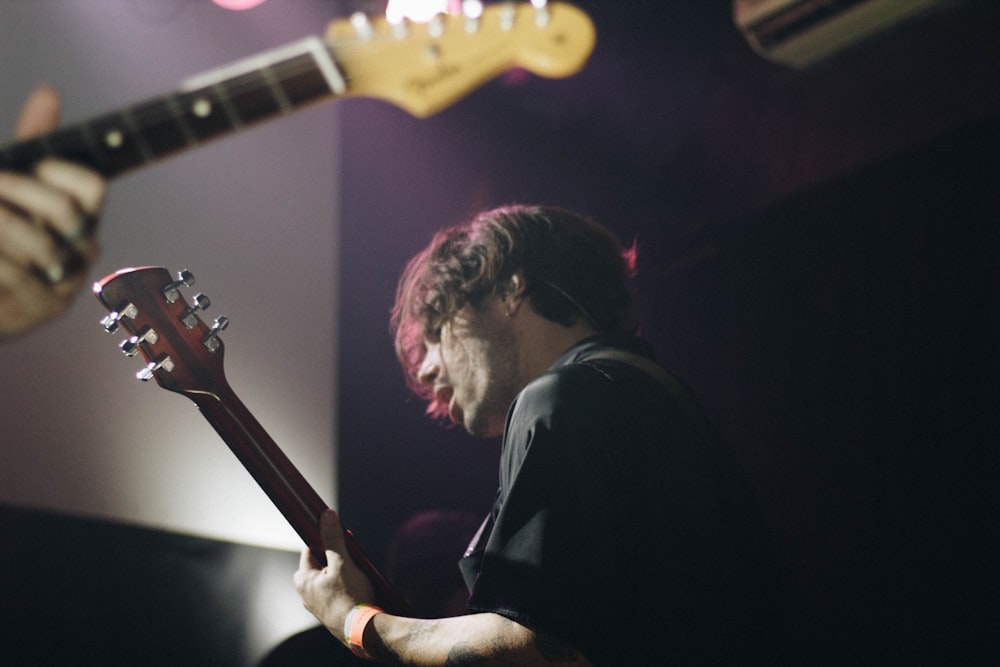 man wearing black shirt standing while playing guitar