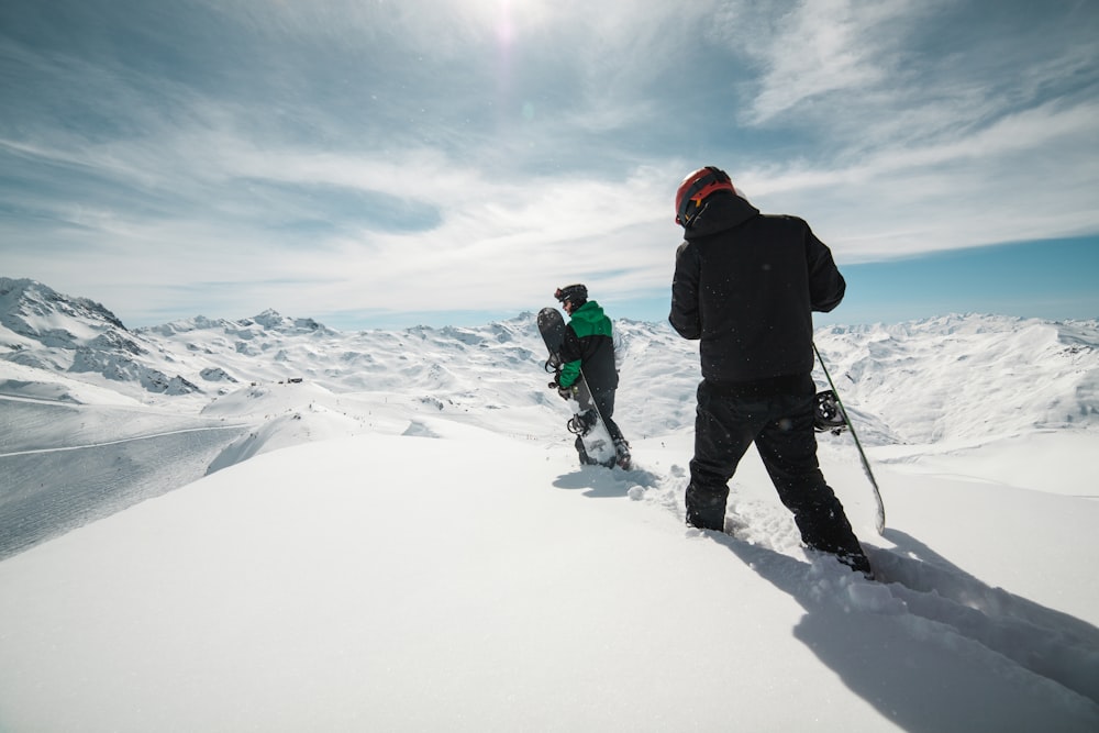 duas pessoas carregando pranchas de snowboard em terreno coberto de neve