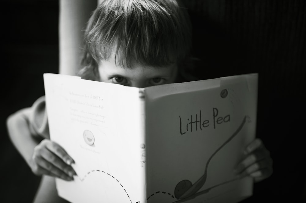 Foto en escala de grises de niño sosteniendo un libro