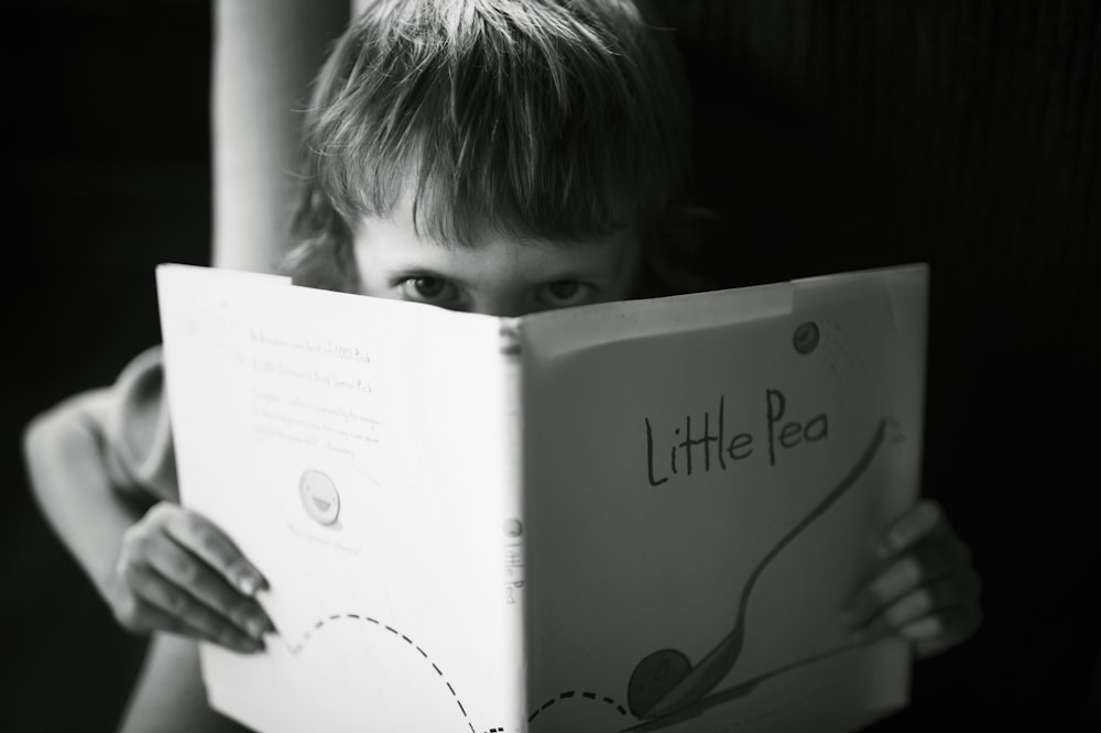 Photo en niveaux de gris d’un garçon tenant un livre