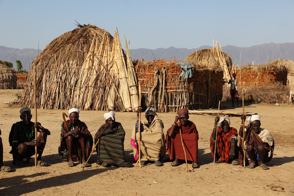 group of tribal men sitting on soil while holding sticks