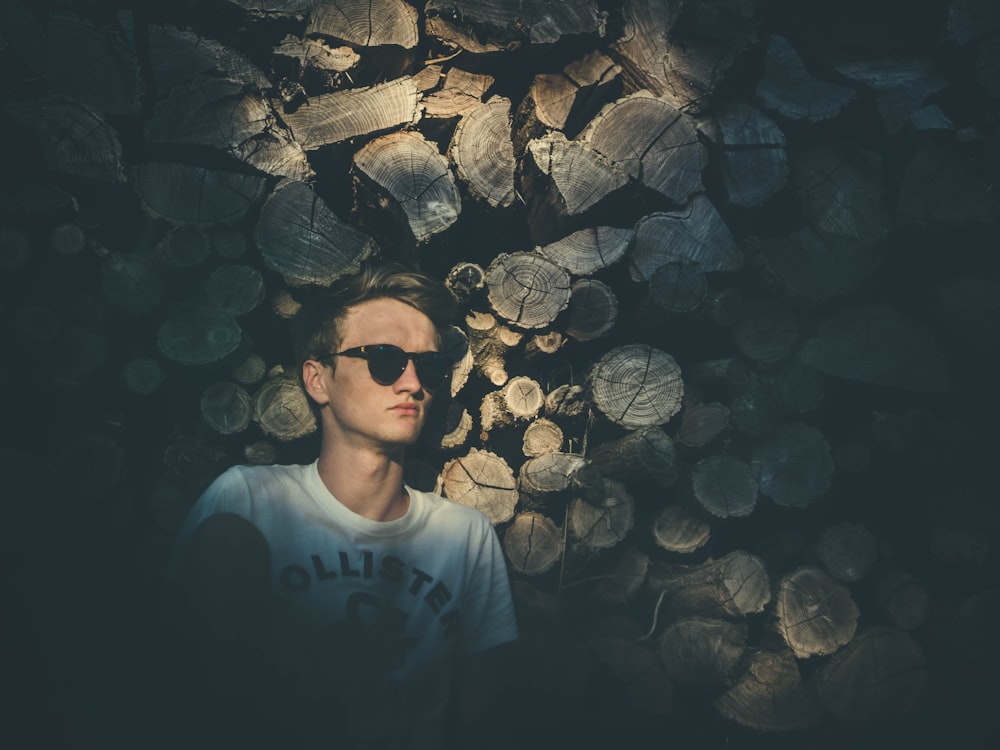 man wearing sunglasses leaning on chopped trees