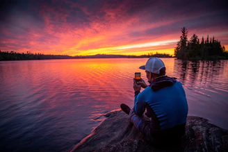 man sitting on gray rock while taking photo of silhouette
