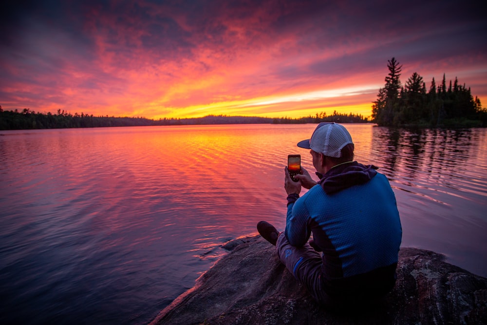 man sitting on gray rock while taking photo of silhouette