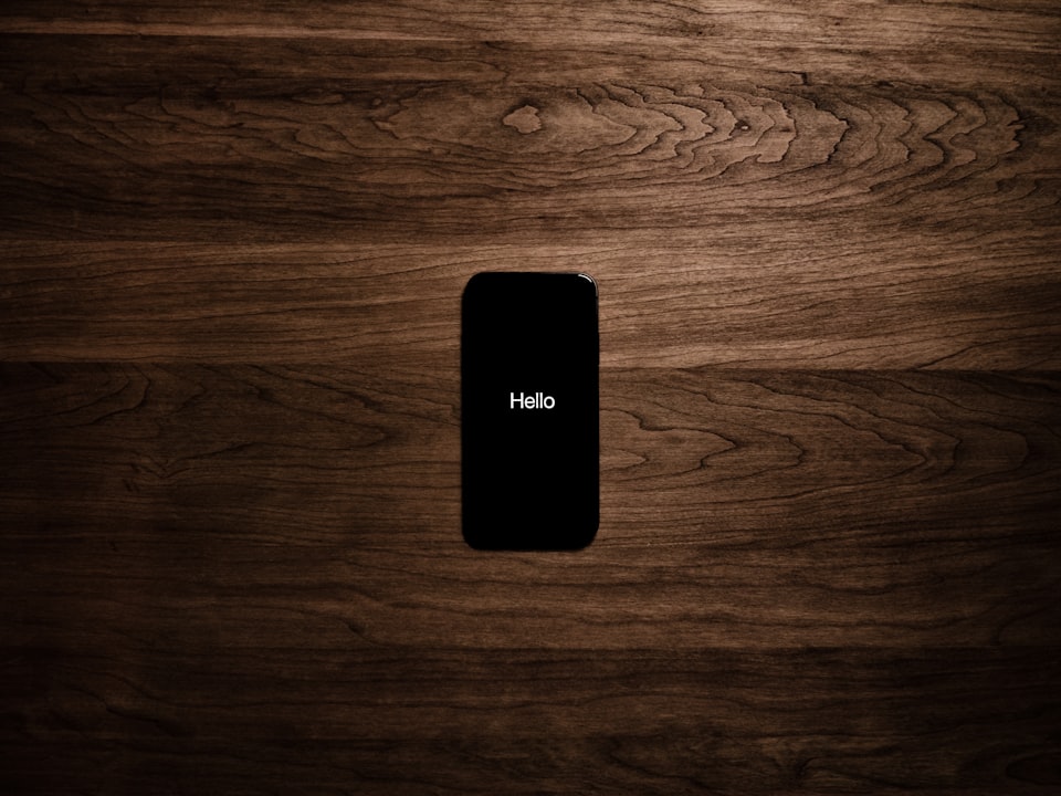 Top-down view of phone on dark wood table, displaying word "Hello".