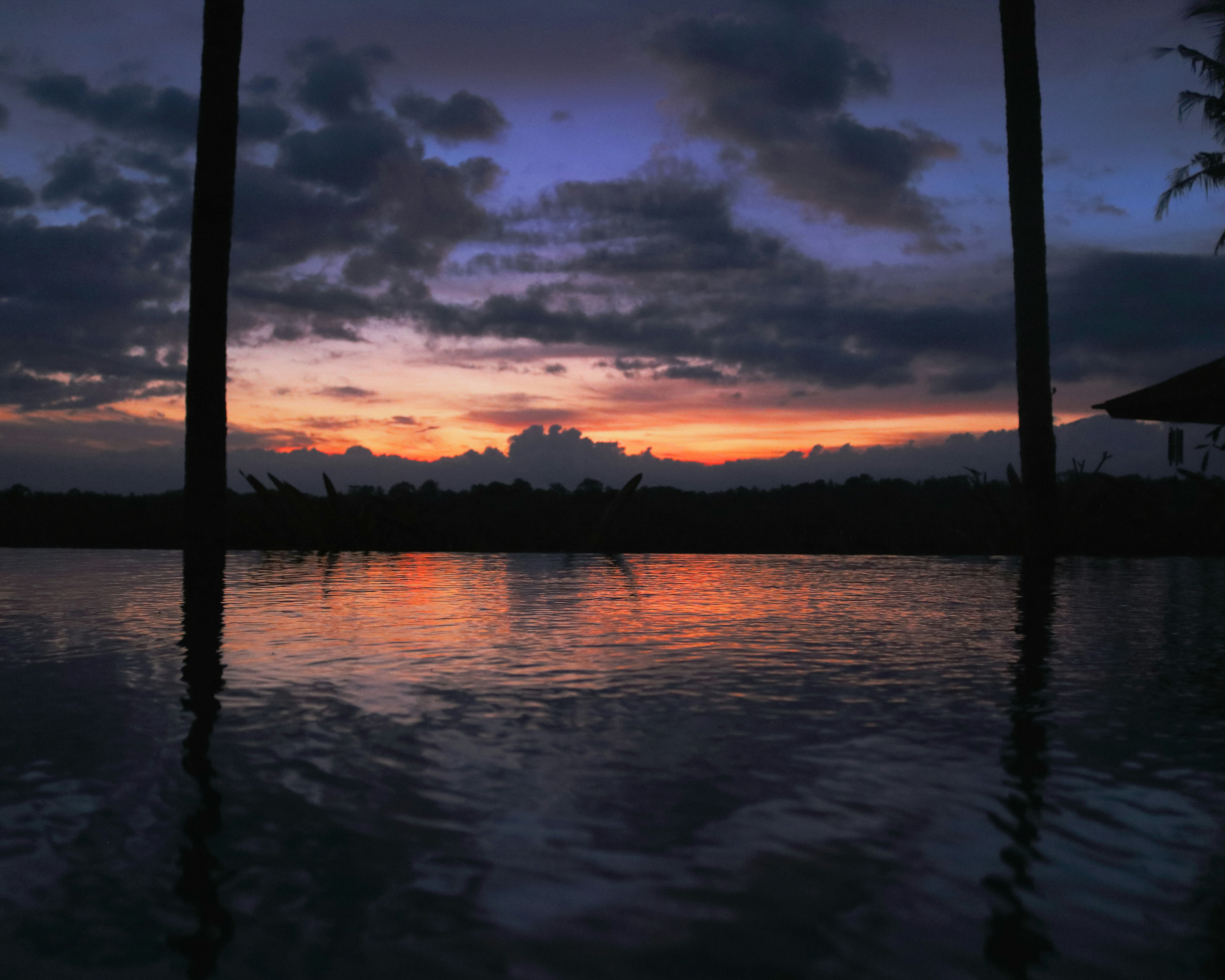 Dramatic Maldives sunset with blazing orange and pink sky reflecting on perfectly calm ocean water, silhouette of palm trees