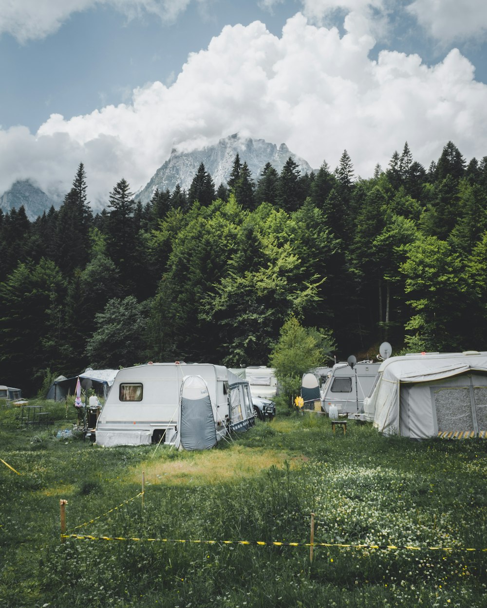 camper trailer near trees with snow-capped mountain at distance