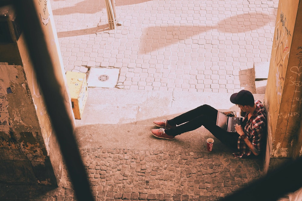 person sitting while using laptop computer on gray concrete floor at daytime