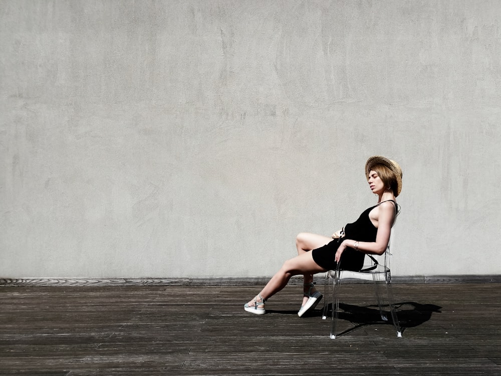 Mulher sentada na poltrona preta perto da parede cinza