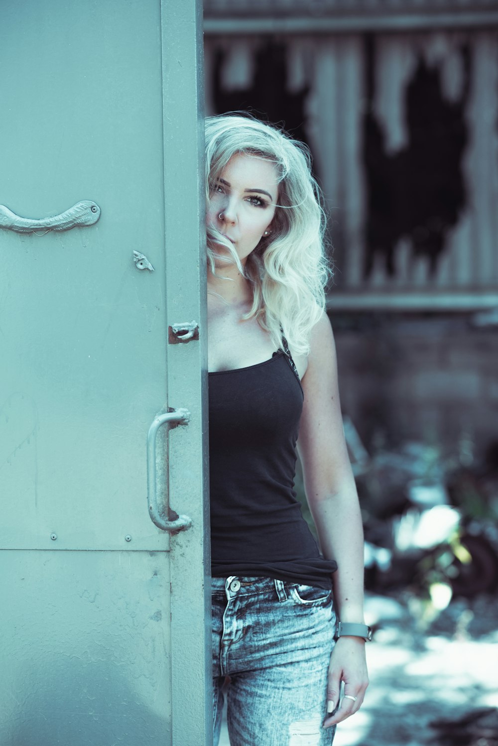 woman in black spaghetti strap top standing behind gray door