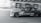 A high-speed car, adorned with racing decals, speeds along a road with a dynamic motion blur effect, emphasizing its velocity. The driver, wearing a helmet, is focused and in full racing gear. The background features an urban setting under a bridge, adding to the sense of motion.