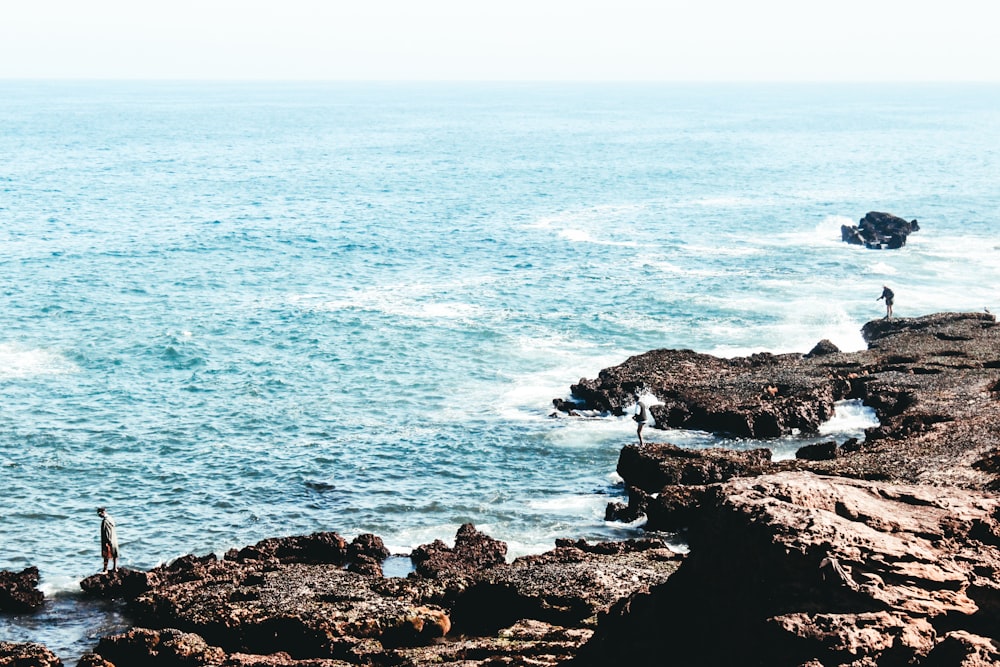 three person standing on rock near the sea during daytime