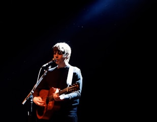 A student performing on stage with a guitar.