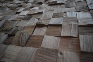 A textured surface composed of various square wooden tiles arranged in a grid pattern. Each tile has distinct grain patterns and shades, creating a three-dimensional appearance.