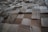 A textured surface composed of various square wooden tiles arranged in a grid pattern. Each tile has distinct grain patterns and shades, creating a three-dimensional appearance.