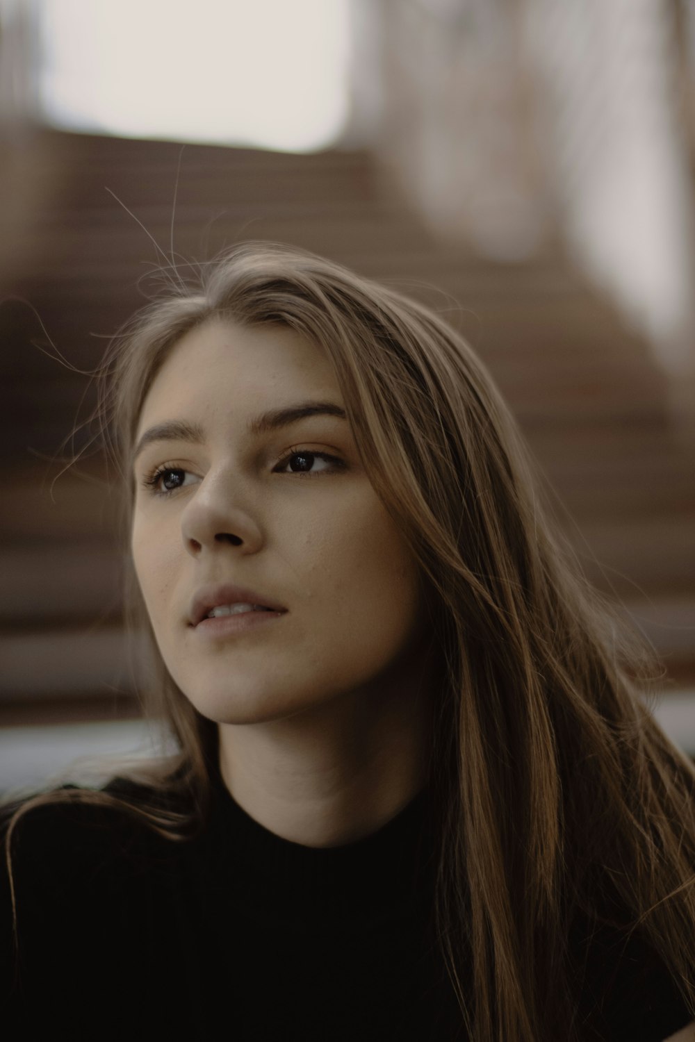 a woman with long hair sitting in front of stairs