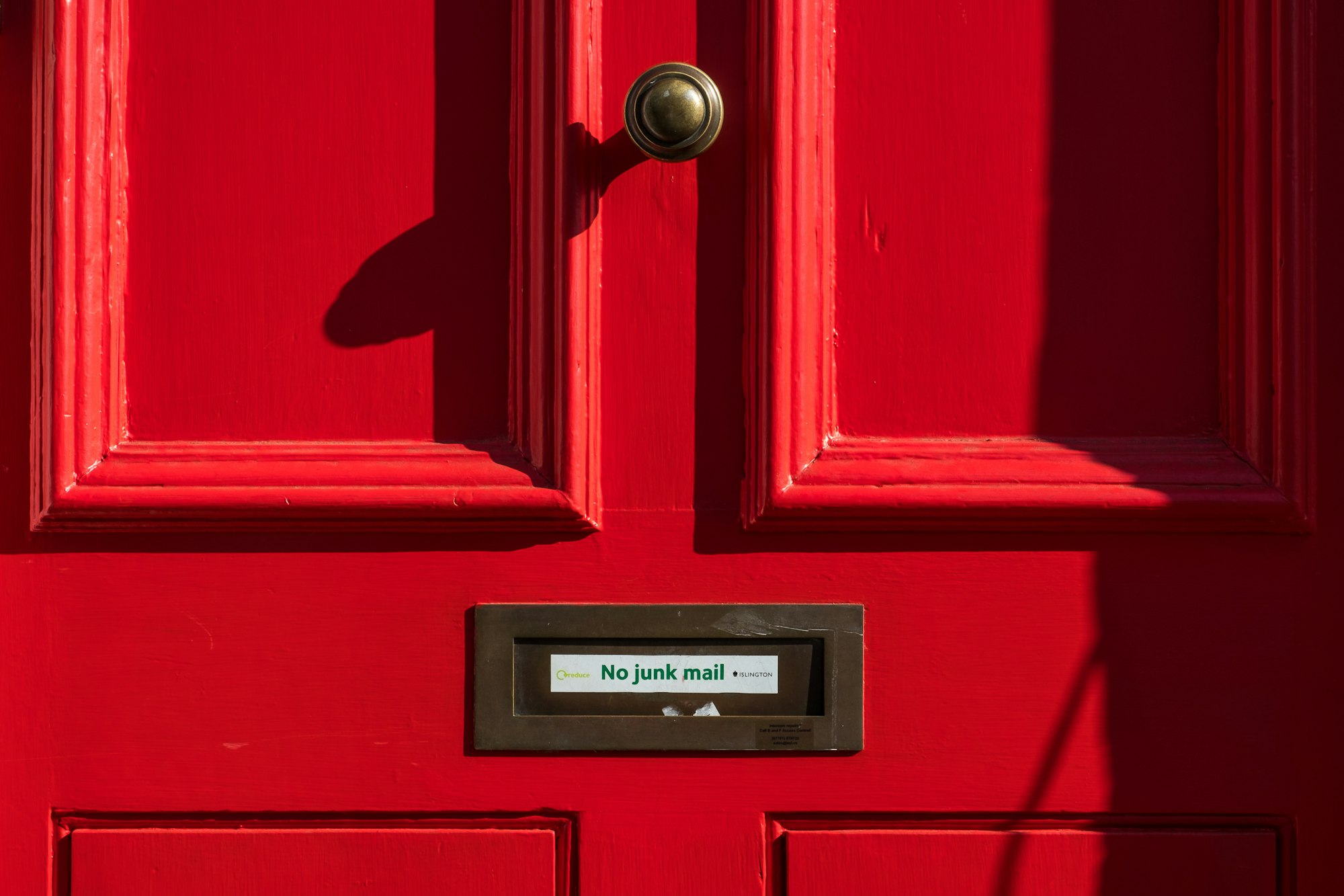 Porta com uma ranhura para correio ao centro onde se lê, num papel colado: "No junk mail". Acima, ao centro, uma maçaneta.