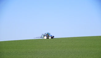 A vibrant tractor working in a lush green field under a clear blue sky.
