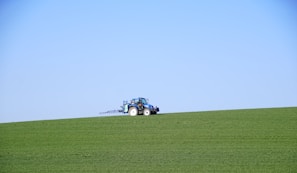 A small tractor carefully spreading gravel along a rural driveway under a bright blue sky
