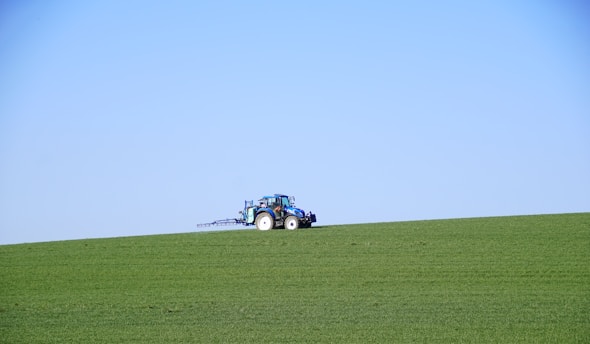 A vibrant green tractor mowing a wide open field under a clear blue sky.