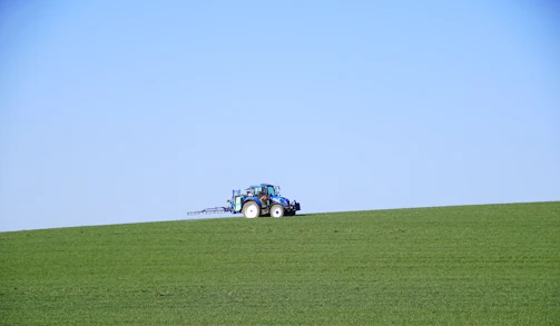 Tractor leveling soil on a rural farm road under clear sky