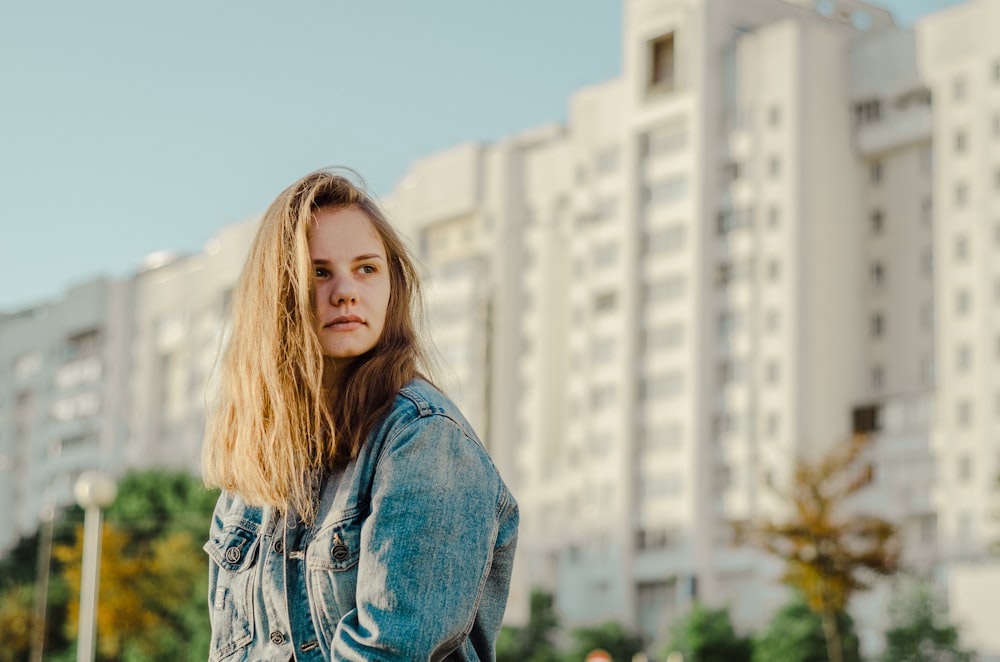 woman wearing blue denim jacket standing in front of white concrete buildings