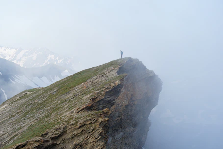 A strong man standing alone on a rocky cliff at dawn, looking out over a vast, misty forest.