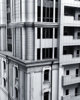 A section of a modern architectural building with intricate designs and vertical lines. The facade includes both art deco elements and modern window designs, featuring a balance of symmetry and ornamental detailing. The structure combines stone and glass materials, giving it a sleek and sophisticated appearance.