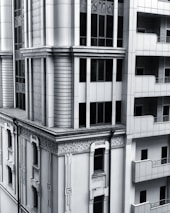 A section of a modern architectural building with intricate designs and vertical lines. The facade includes both art deco elements and modern window designs, featuring a balance of symmetry and ornamental detailing. The structure combines stone and glass materials, giving it a sleek and sophisticated appearance.