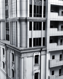 A section of a modern architectural building with intricate designs and vertical lines. The facade includes both art deco elements and modern window designs, featuring a balance of symmetry and ornamental detailing. The structure combines stone and glass materials, giving it a sleek and sophisticated appearance.