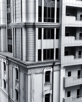 A section of a modern architectural building with intricate designs and vertical lines. The facade includes both art deco elements and modern window designs, featuring a balance of symmetry and ornamental detailing. The structure combines stone and glass materials, giving it a sleek and sophisticated appearance.