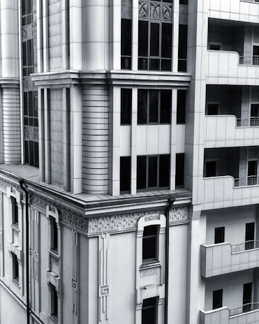 A section of a modern architectural building with intricate designs and vertical lines. The facade includes both art deco elements and modern window designs, featuring a balance of symmetry and ornamental detailing. The structure combines stone and glass materials, giving it a sleek and sophisticated appearance.
