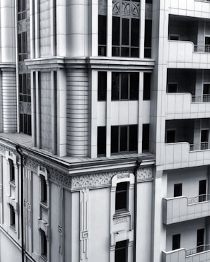 A section of a modern architectural building with intricate designs and vertical lines. The facade includes both art deco elements and modern window designs, featuring a balance of symmetry and ornamental detailing. The structure combines stone and glass materials, giving it a sleek and sophisticated appearance.