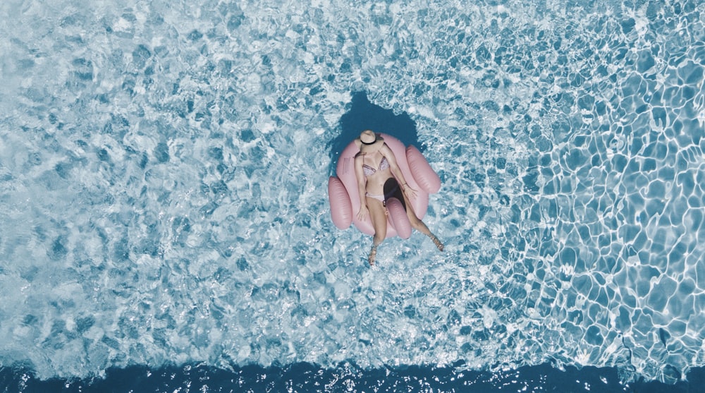 Femme sur une bouée rose entourée d’un plan d’eau pendant la journée