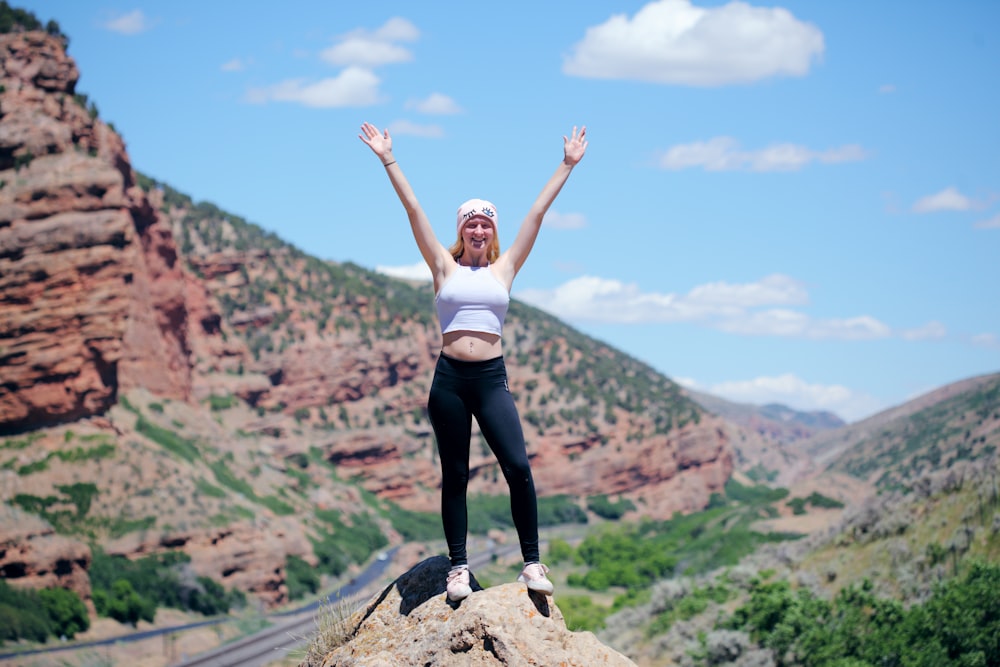 woman wearing white top and black pants standing on cliff