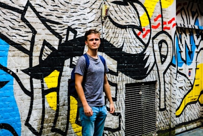Smiling youth holding books and sports gear, standing proudly in front of a colorful mural.
